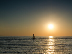 Segelboot auf dem Meer vor einer untergehenden Sonne und orangegefärbtem Himmel