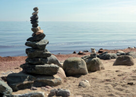 Turm aus aufeinandergestapelten Steinen am Strand mit Meer im Hintergrund