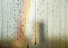 Blick durch eine Scheibe voller Regentropfen mit unscharfen Turm und Regenbogen im Hintergrund